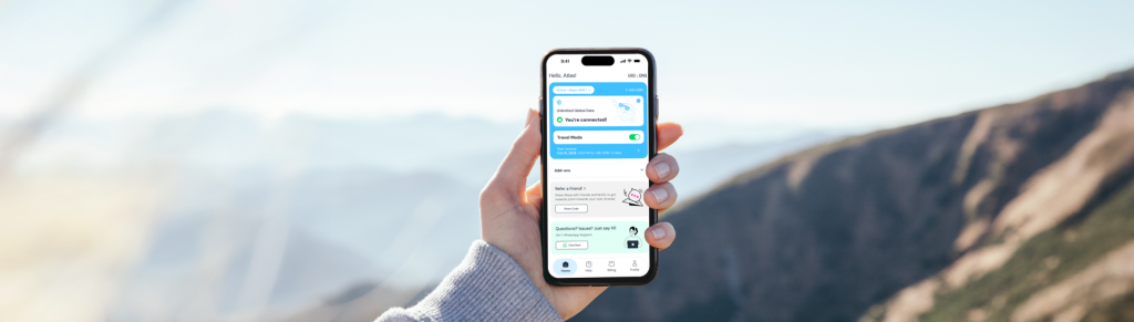 Mountains as background, hand holding iPhone showing with Maya Mobile Travel Mode App
